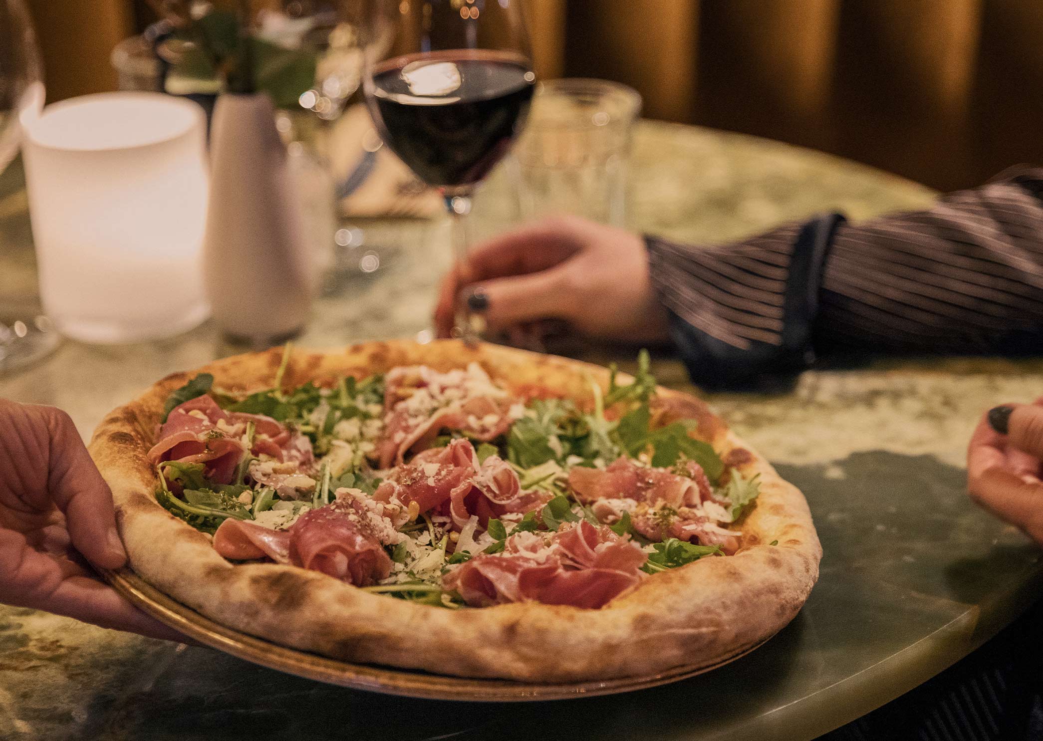 Pizza topped with cured ham and arugula, served with a glass of red wine.