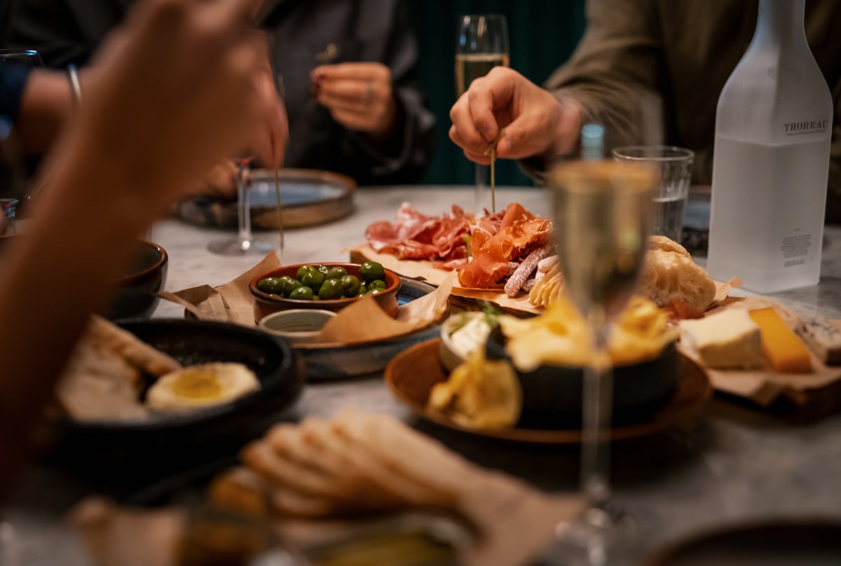 People sharing a charcuterie board with cheeses, cured meats and olives, served with sparkling wine.